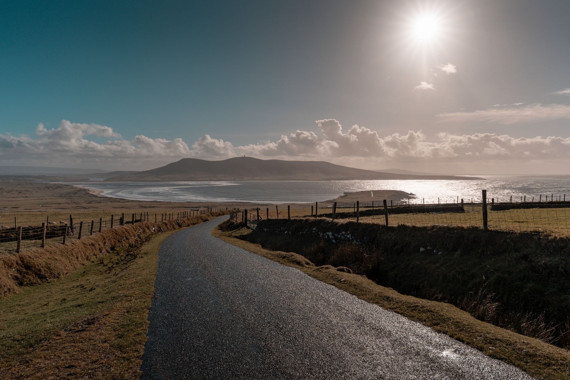 A coastal road curving along the Irish shoreline under a soft, clear sky